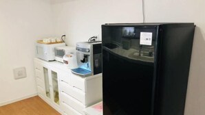 Eine Küchenzeile mit einem schwarzen Kühlschrank, einer Mikrowelle, einer Kaffeemaschine und einer kleinen Arbeitsplatte mit Einmachgläsern.