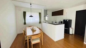 Eine kompakte Küche mit einer zentralen Kochinsel, einem Essbereich mit Holztisch und Stühlen sowie einem schwarzen Spiegel über der Insel.