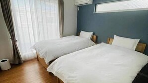 Ein Hotelzimmer mit zwei Betten, Holzboden, einem fenster mit Vorhängen und einer Klimaanlage an der Wand.