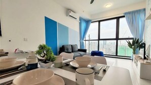 A modern living room with a dining area, large windows with curtains, and a view of the cityscape. - Skyblue 2 Rooms Apartment, 4+2 Pax @ Urban Suites (George Town)