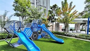 A playground with slides and climbing structures in a park area with grass and trees. - Skyblue 2 Rooms Apartment, 4+2 Pax @ Urban Suites (George Town)