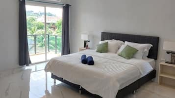A hotel room with a bed, a nightstand, a lamp, and a view of greenery through the window.