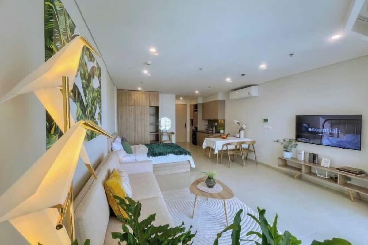 A modern living room with a sofa, a dining table, a TV, and a kitchen area.