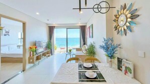 A modern hotel room with a balcony, a dining area, and a decorative wall clock. - The Song Vung Tau - Hong Hanh Apartments (Vung Tau)