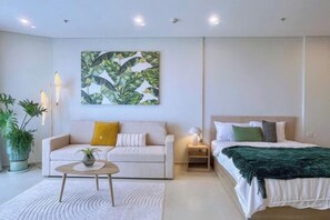 Une chambre à coucher moderne, avec un lit, un canapé, une table basse et un tableau accroché au mur.