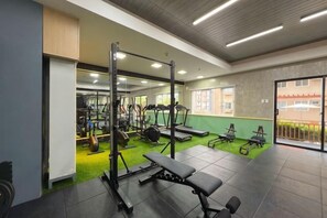 Academia com equipamentos de ginástica, um banco e uma área coberta por carpete verde.