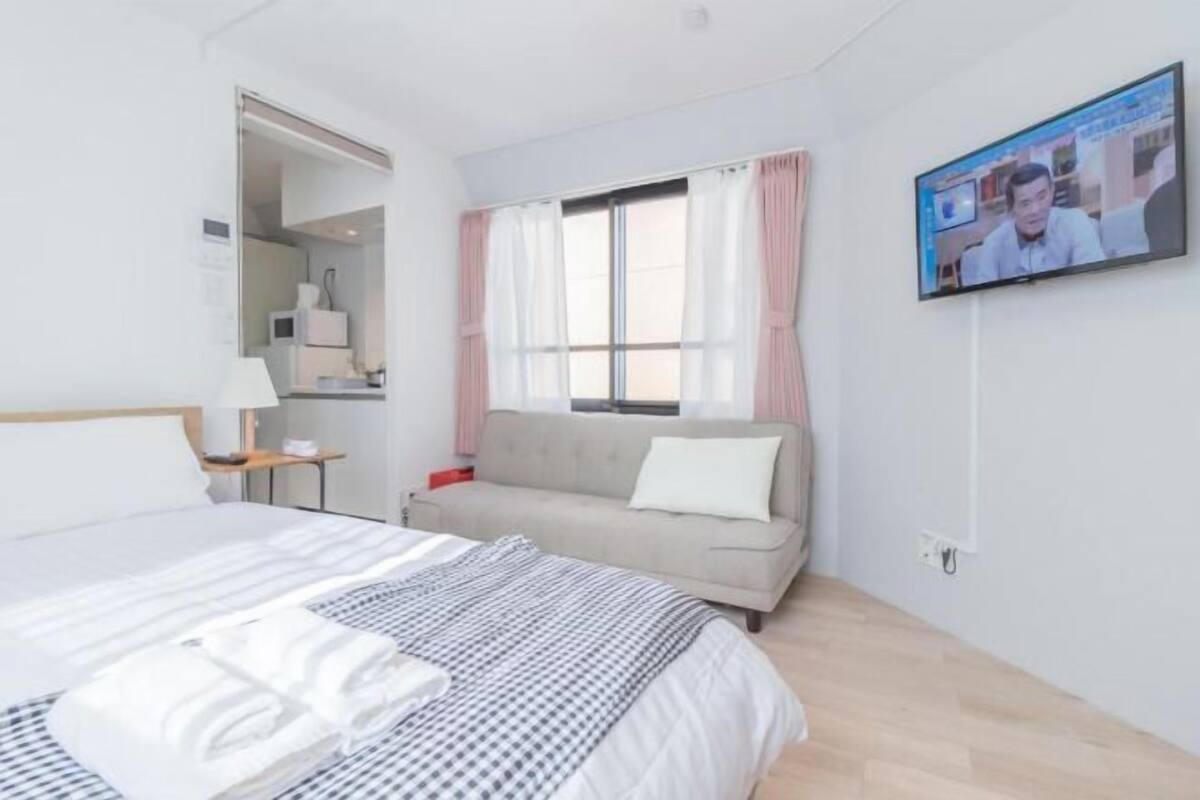 Hotellihuone, jossa on sänky, sohva, televisio ja ikkuna, jossa on verhot.