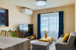 Ett hotellrum med en tv, ett matbord, en soffa och ett fönster med gardiner.