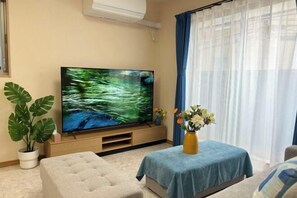 Ett vardagsrum med en platt-TV, en soffa, ett soffbord, en krukväxt och en vas med blommor.