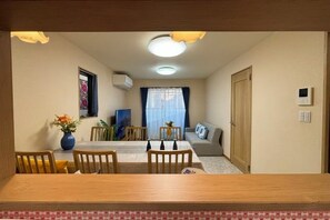 En matplats med ett träbord och stolar, en vas med blommor, en soffa och ett fönster med gardiner.