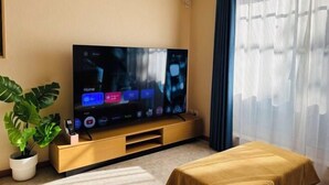 A modern hotel room with a flat-screen TV on a wooden stand, a potted plant, and a bed with a yellow bedspread. - Lapis House 201 2F&3F (Tokyo)