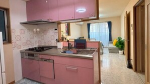 A compact kitchen with pink cabinets, a gas stove, and a sink. - Lapis House 201 2F&3F (Tokyo)
