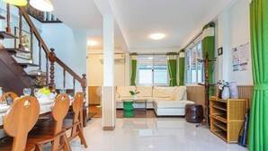 A spacious living area with a staircase, a dining table with chairs, a sofa, and a bookshelf. - Friend House BKK (Bangkok)