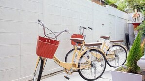 A yellow bicycle with a red basket and a brown seat parked against a white wall. - Friend House BKK (Bangkok)