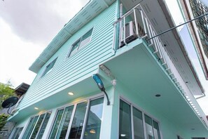 A multi-story building with a light blue exterior, large windows, and a visible balcony. - Friend House BKK (Bangkok)