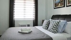 Un lit bien fait, recouvert d’une couverture grise, avec deux oreillers à motifs en zigzag et une serviette blanche enroulée posée sur un oreiller blanc.