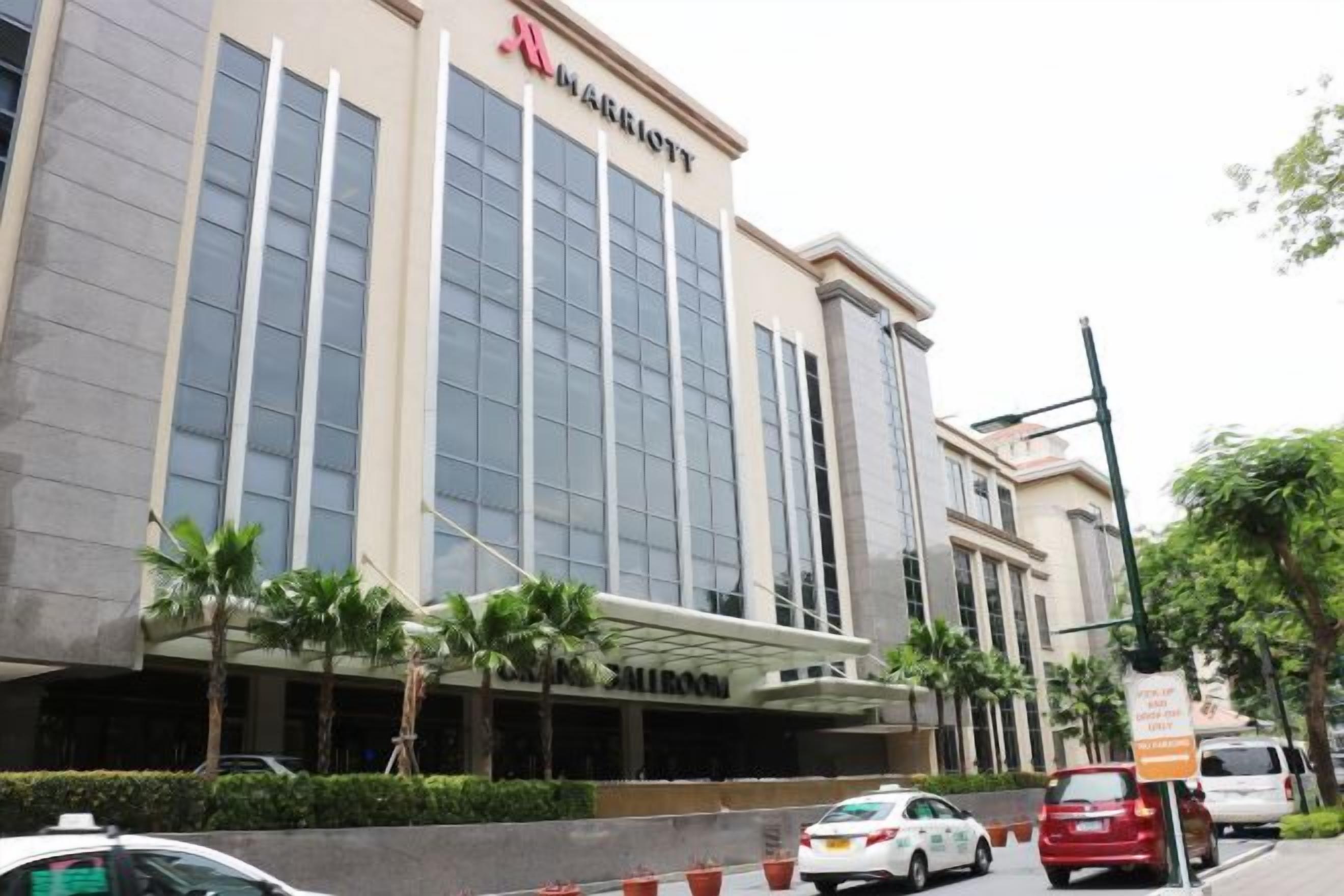 A multi-story hotel with a prominent sign, a covered entrance, and a parking area with cars.