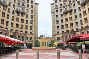 A courtyard with a central fountain, surrounded by outdoor seating with umbrellas, and high-rise buildings in the background.