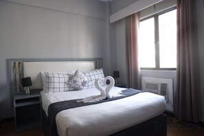 Een net opgemaakt bed met een zwaan decoratie, een nachtkastje met een lamp, en een raam met gordijnen.