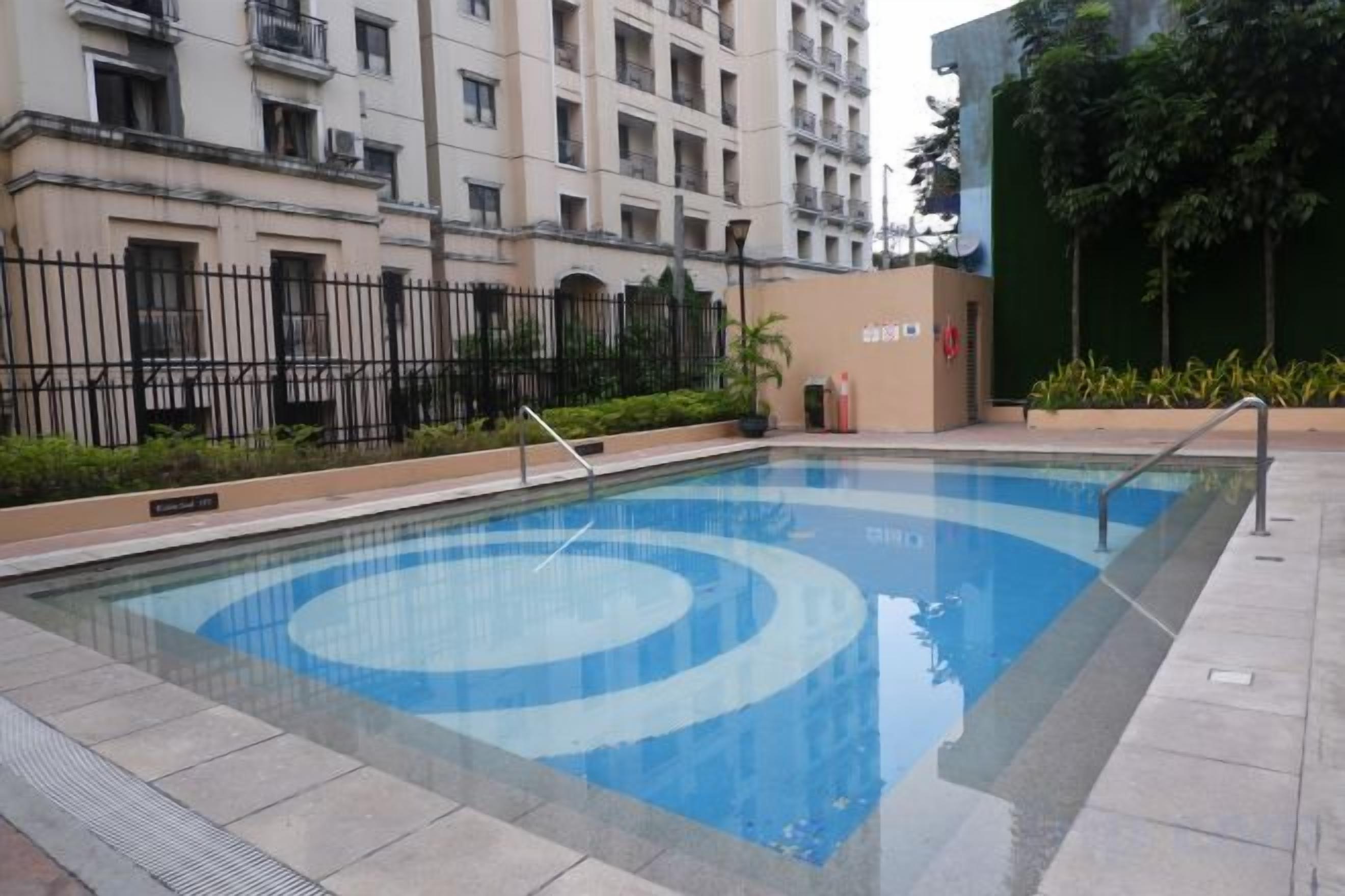 Una piscina con diseño circular, rodeada por una valla y un edificio al fondo.