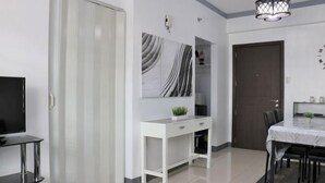 Un salon moderne avec une console blanche, un téléviseur à écran plat, une table à manger avec des chaises et une porte sombre.