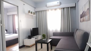 Un salon moderne avec un canapé, un téléviseur, une petite table et un lit dans la pièce adjacente.