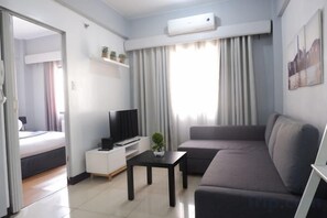 Una sala de estar moderna con un sofá, un televisor sobre un mueble bajo, una mesita y una ventana con cortinas.