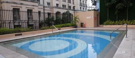 Une piscine aux motifs bleus et blancs, entourée d’une zone pavée et d’une clôture.
