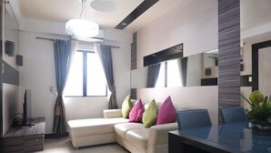 A modern living room with a sectional sofa, a glass dining table, and a large mirror. - Sarasota Residential Resort by SMTL Properties (Pasay)