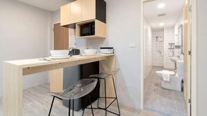A compact kitchen with a wooden countertop, two bar stools, a microwave, and a sink.