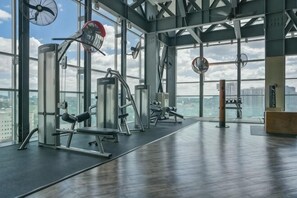 Un gimnasio con equipo de ejercicios, ventanas amplias y vista a la ciudad.