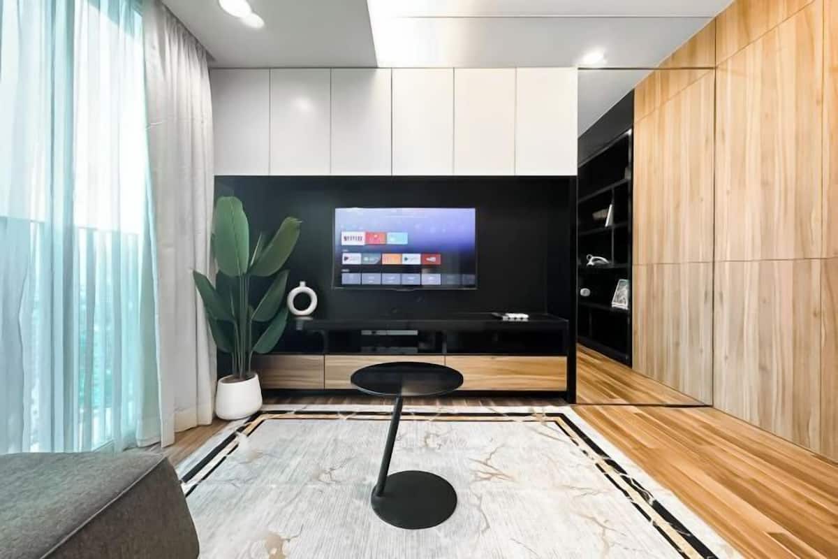 Un moderno salón con un televisor de pantalla plana montado en una pared de madera, una mesa de centro redonda y una planta grande en maceta.