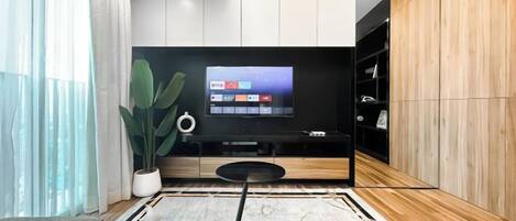 A modern living room with a flat-screen TV mounted on a wooden wall, a round coffee table, and a large potted plant.