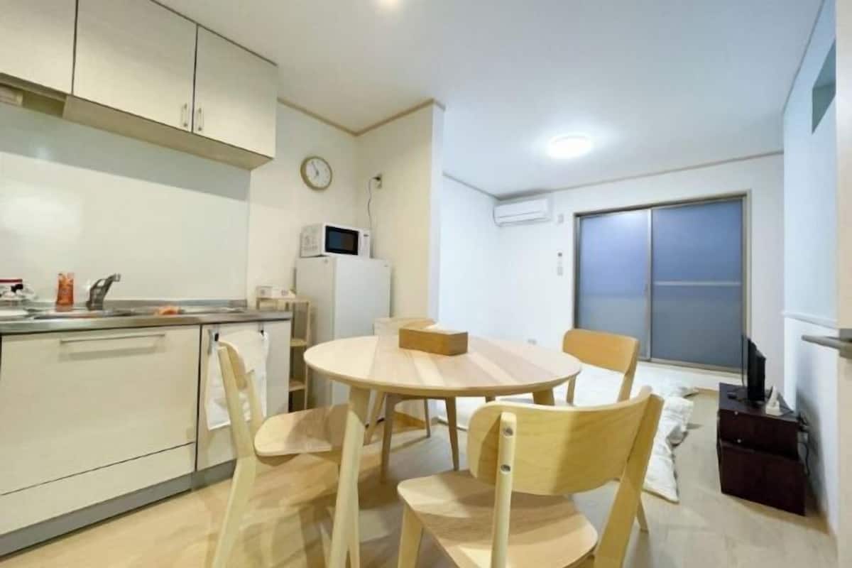 Una cocina compacta con una mesa y sillas, microondas y un reloj en la pared.
