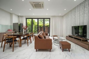 A modern living room with a sofa, dining table, chairs, a TV, and a kitchen area.