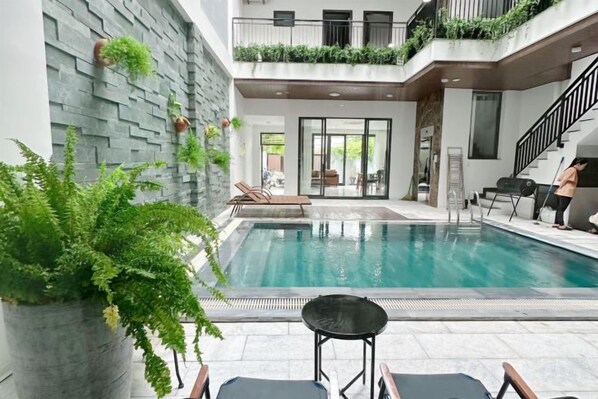 A modern indoor pool area with a lounge chair, a small table, and a staircase leading to an upper level.