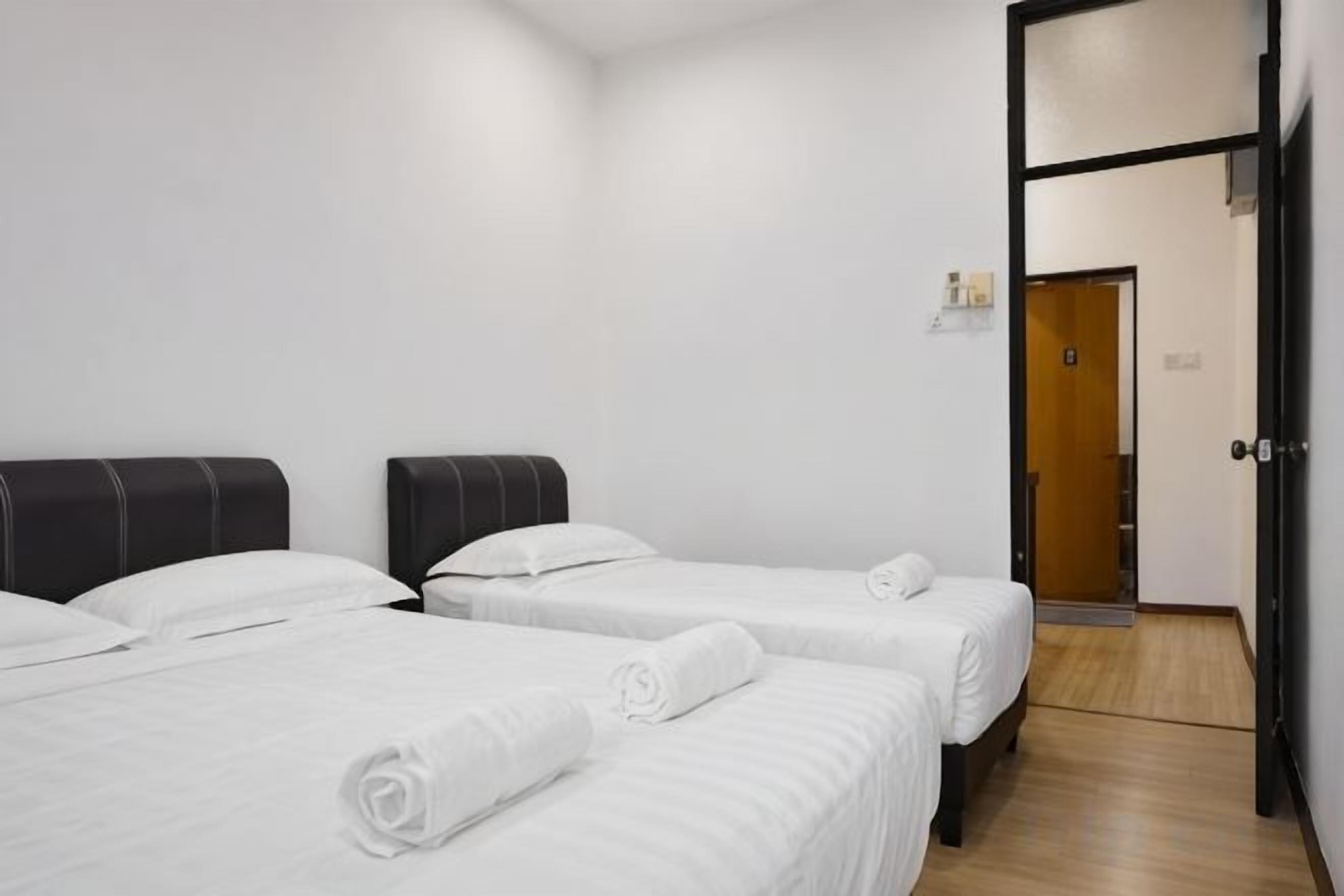 A hotel room with two beds, a wooden floor, and a door leading to a hallway.