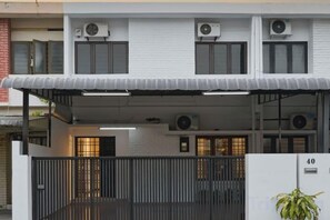 Un edificio de dos pisos con un porche cubierto, unidades de aire acondicionado y un camino de entrada con portón.