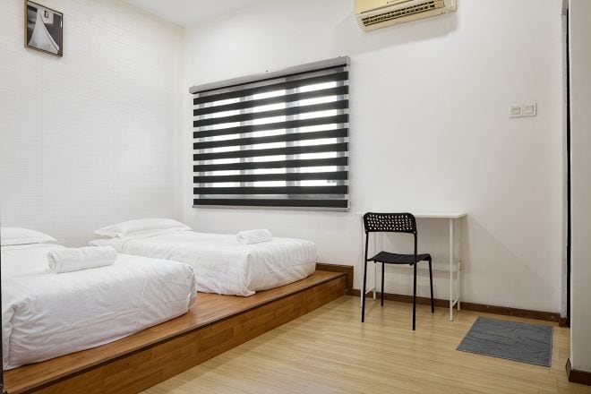 A room with two beds, a desk, a chair, and a window with blinds.