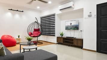 A modern living room with a sofa, red bean bag, hanging chair, TV, and wooden cabinet.