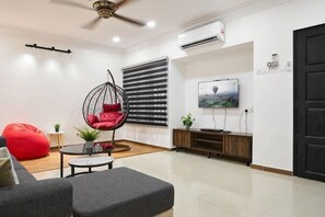 Ein modernes Wohnzimmer mit einer Couch, einem roten Sitzsack, einem Hängekorbsessel, einem Fernseher und einer Holzkommode.
