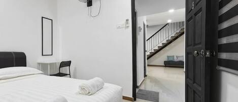 A bedroom with a bed, bedside table, and a fan. There is a door leading to a staircase.