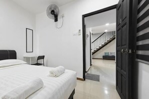 Een slaapkamer met een bed, een bureau, een stoel, een ventilator en een deur die naar een trap leidt.
