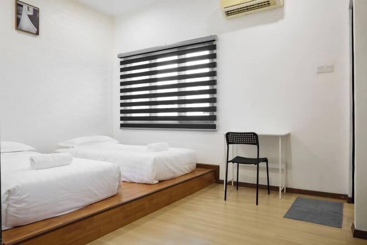 A hotel room with two single beds, a desk, a chair, and a window with blinds.