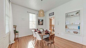 A dining area with a wooden table, white chairs, a hanging light fixture, and a shelf with decorative items. - Moment in Time - Hot Tub & Fire Pit (Fredericksburg)
