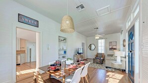 A dining area with a wooden table, white chairs, and a hanging light fixture. - Moment in Time - Hot Tub & Fire Pit (Fredericksburg)