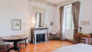 A room with a round wooden table, a fireplace, a bed, and a window with curtains. - Domaine de la Grotte (Wine Estate) (Sore)