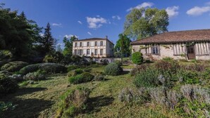 A traditional building with a symmetrical facade, a well-maintained garden with various shrubs and a clear sky. - Domaine de la Grotte (Wine Estate) (Sore)