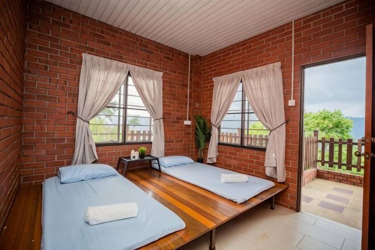 Une chambre avec deux lits, un plancher en bois, des murs en briques et une vue sur l’extérieur grâce à une porte vitrée.