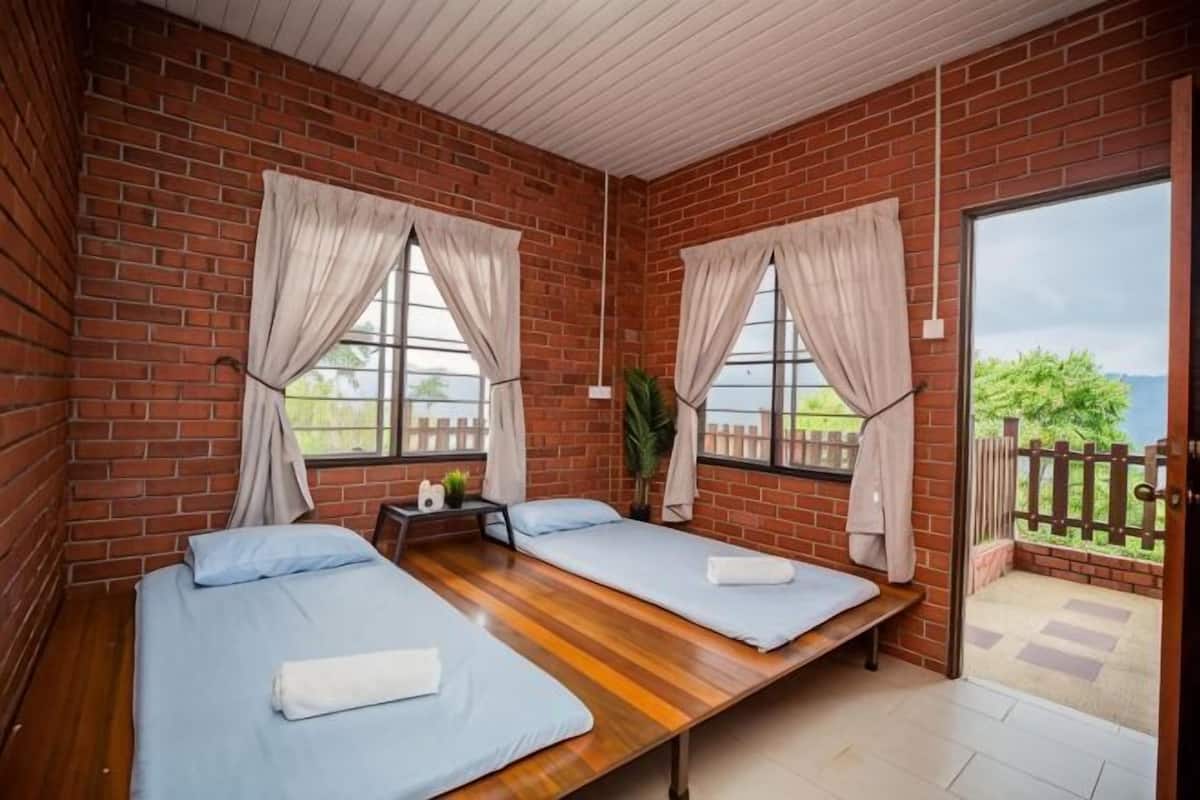 A room with two beds, a wooden floor, brick walls, and a view through a glass door.